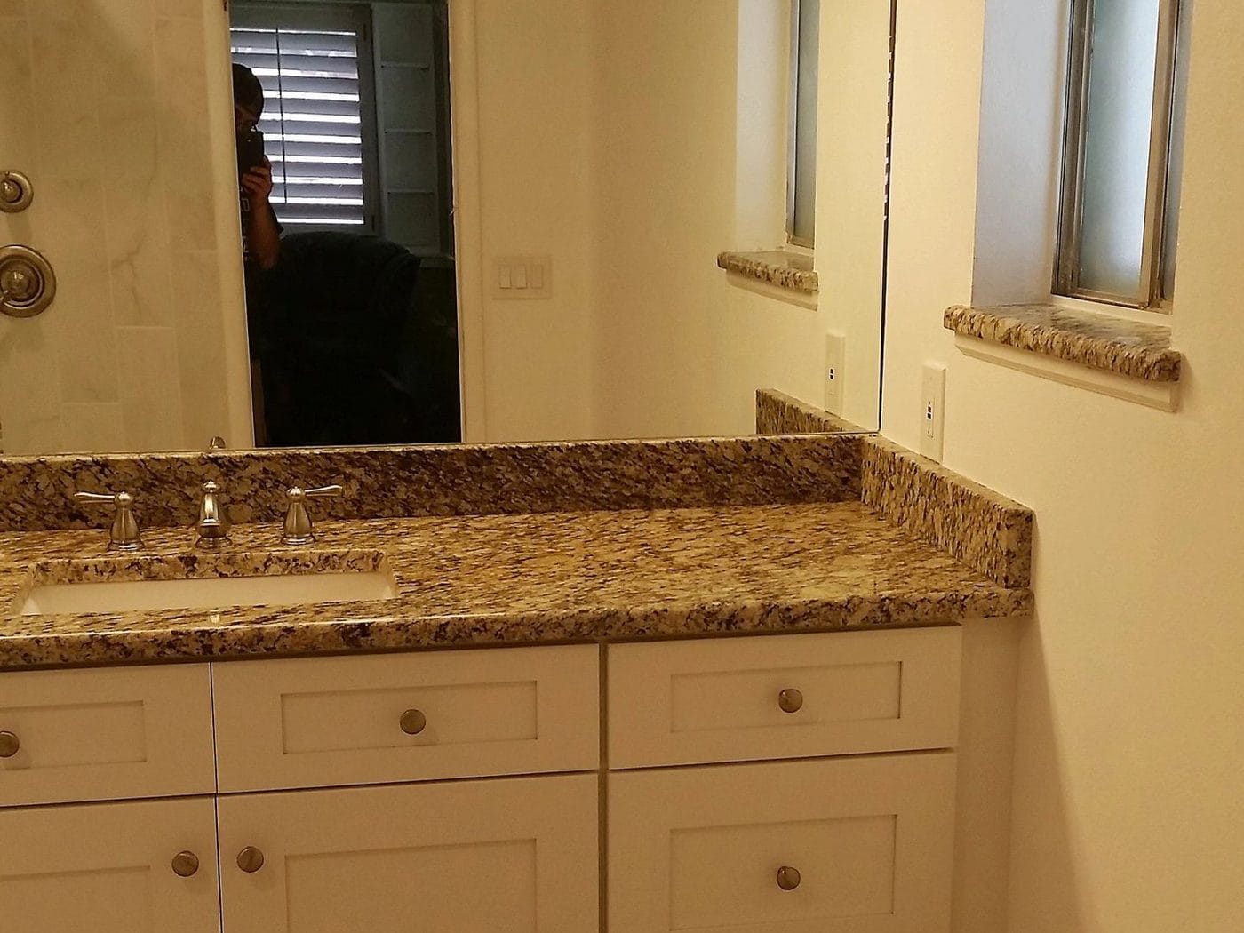 Vanity run with a granite top and a full-width mirror over it